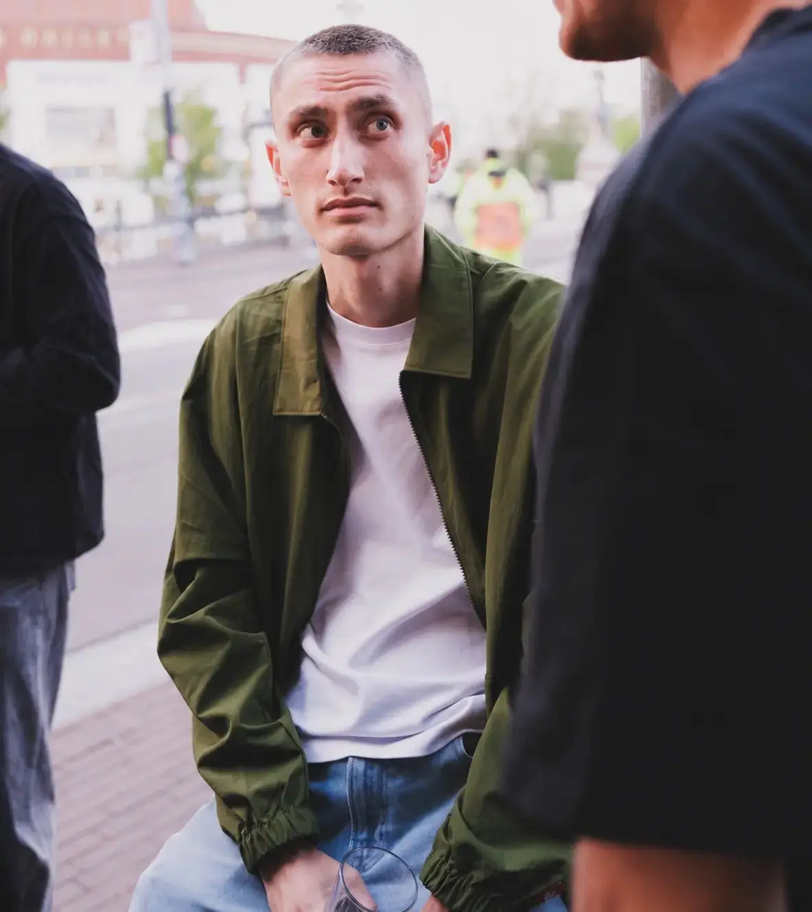 Augustijn Snoep sitting outdoors in an olive jacket and white t-shirt, looking up in conversation